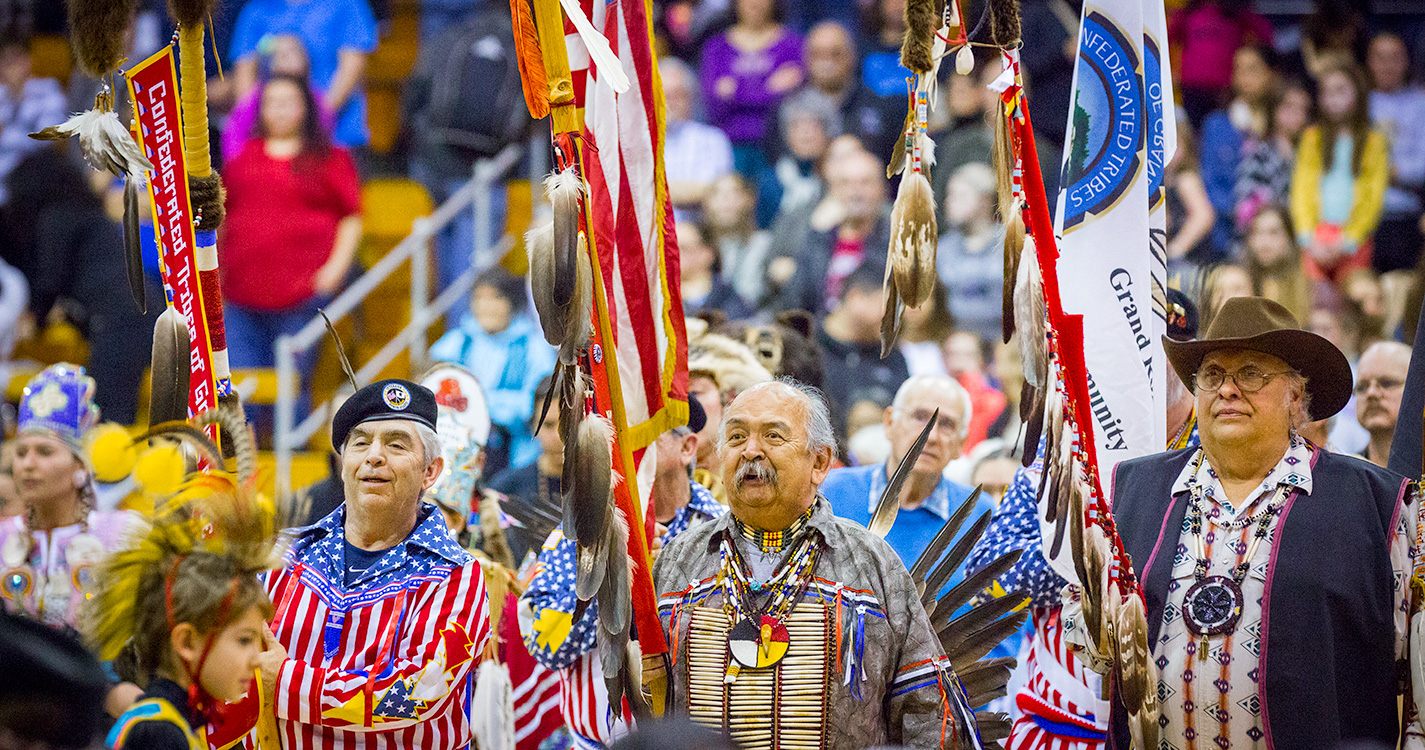 Men in traditional regalia hold flags during the Grand Entrance at the annual Social Pow wow.