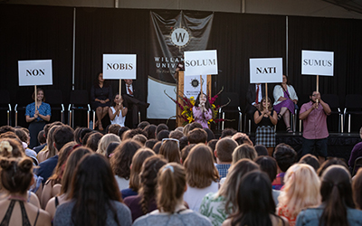 From the crowd's perspective on the Quad, five student hold signs of Willamette's motto in Latin: non nobis solum nati sumus