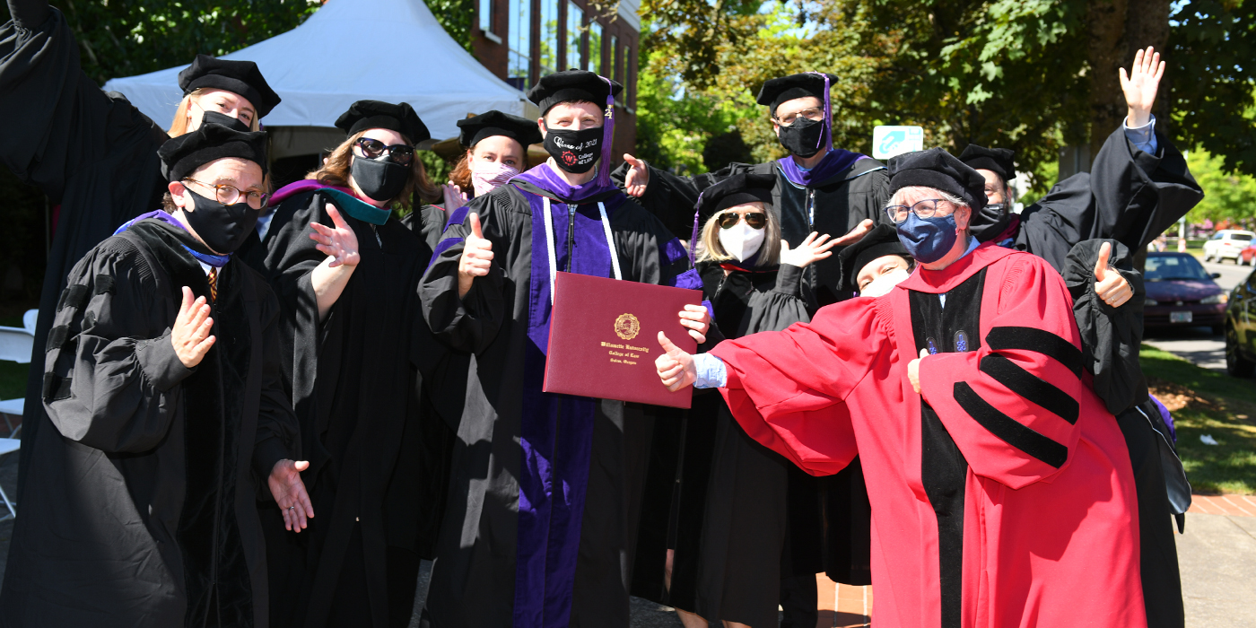Law graduate surrounded by faculty all giving thumbs up